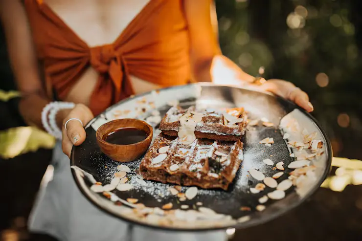 woman-brown-bra-holds-plate-with-waffles-chocolate-sauce-peanuts